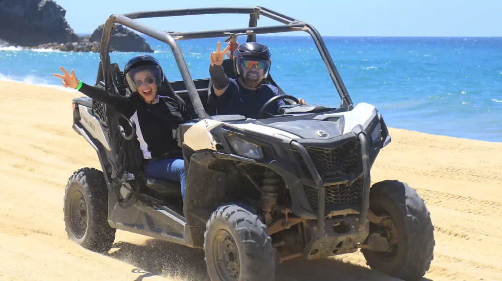 Couple enjoying a Side by Side UTV tour on the beach in Los Cabos with the ocean in the background