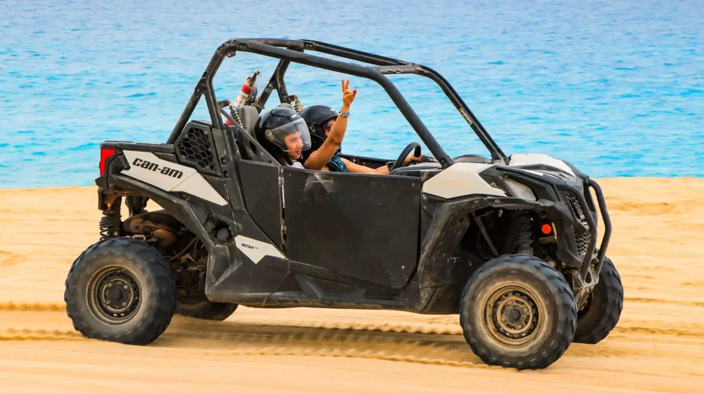 Couple enjoying a Side by Side UTV ride on the beach in Los Cabos with the ocean in the background