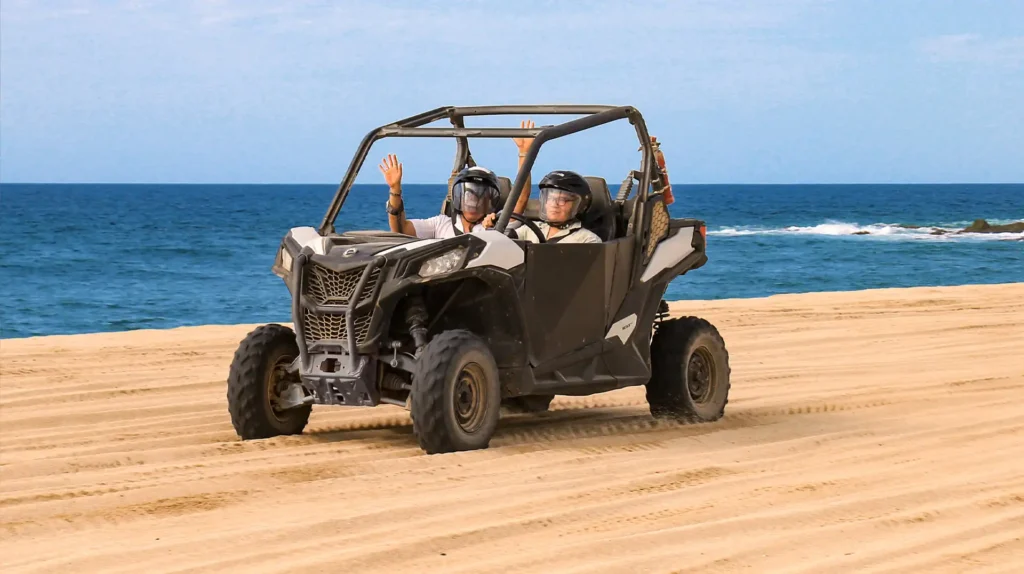 Two people driving a Side by Side UTV on the beach in Los Cabos with the blue ocean in the background