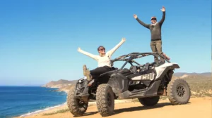 Couple celebrating on top of Can-Am Maverick X3 with ocean view during off road tour in Los Cabos