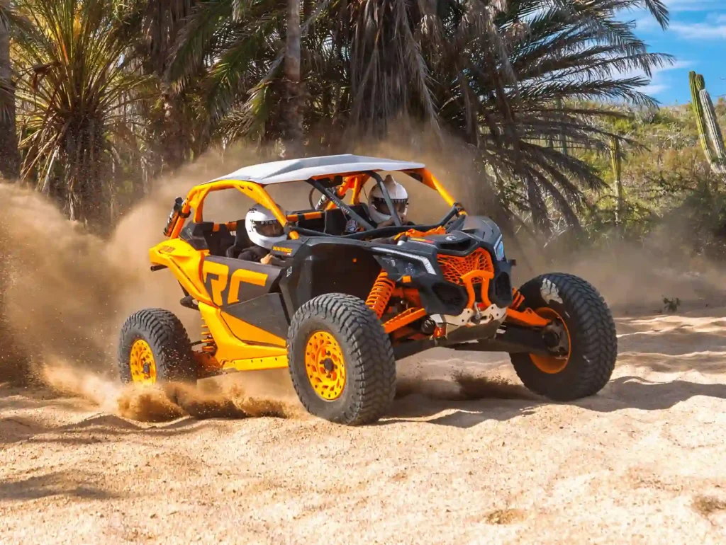 Orange Maverick RC UTV driving through sandy desert trails, kicking up dust among palm trees and vegetation.