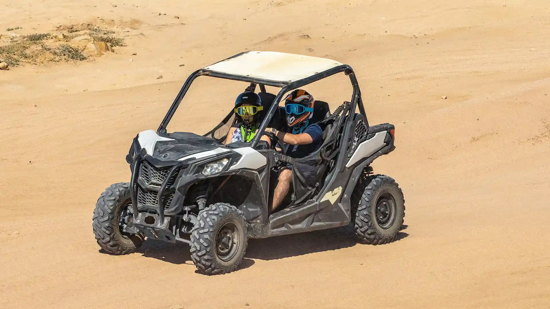 Couple driving a Side by Side UTV through the desert in Los Cabos wearing helmets and safety goggles